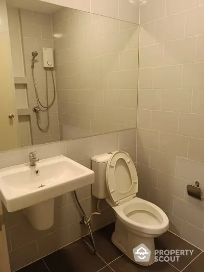 Compact and clean bathroom with wall-mounted sink, toilet, and shower, featuring neutral tile work and practical design.