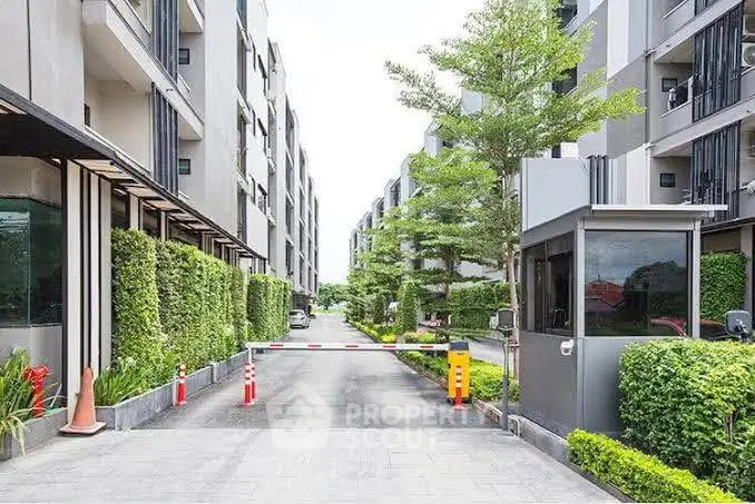 Modern residential complex entrance with lush greenery and security booth