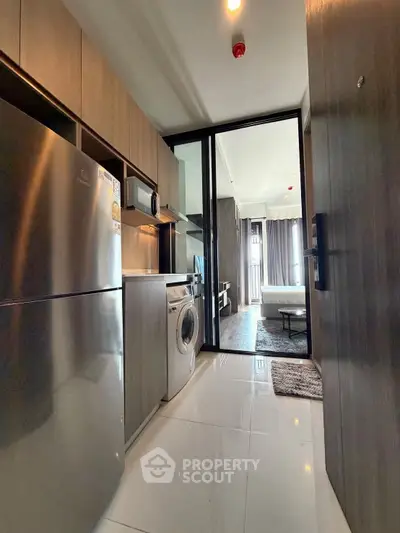 Modern kitchen with stainless steel appliances and washing machine in sleek apartment.