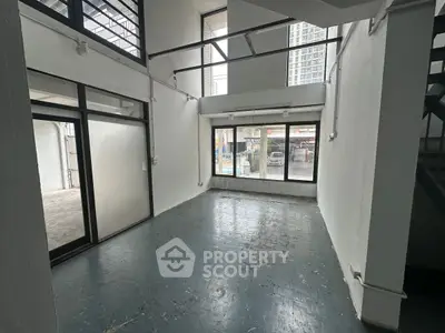 Spacious industrial-style room with high ceilings and large windows in urban setting.