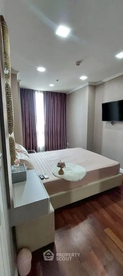 Cozy bedroom with modern decor and natural light, featuring a wall-mounted TV and elegant curtains.