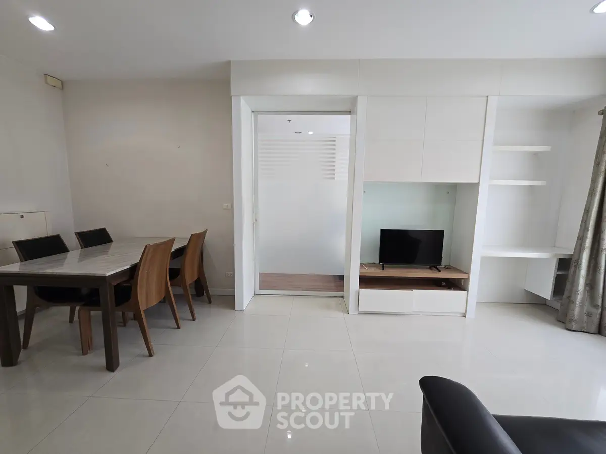 Modern living room with dining area and TV setup, featuring sleek furniture and bright lighting.