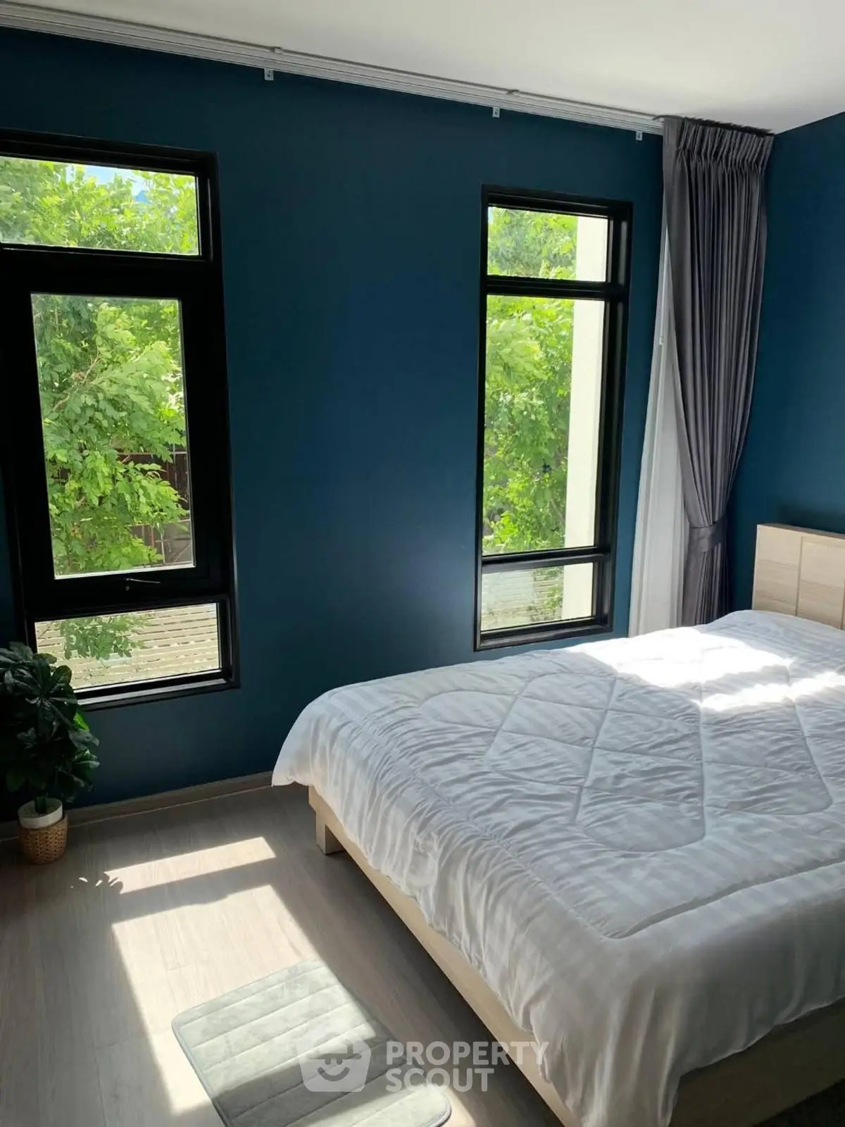 Bright bedroom with large windows and modern decor, featuring a cozy bed and lush green views.