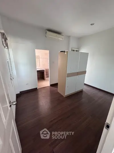 Spacious bedroom with wooden flooring and air conditioning, featuring a wardrobe and bathroom access.