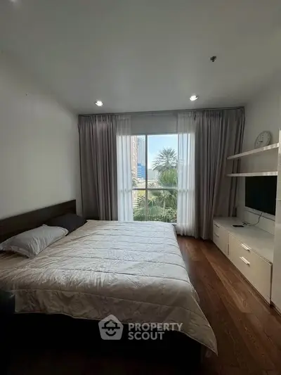 Spacious bedroom with large window offering city view, modern furnishings, and ample natural light.
