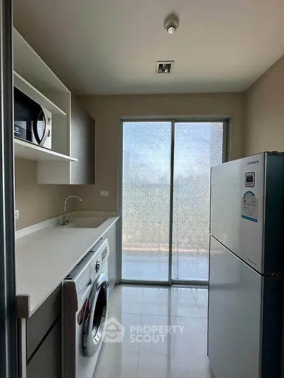 Modern kitchen with washing machine, microwave, and fridge in a bright, compact space.