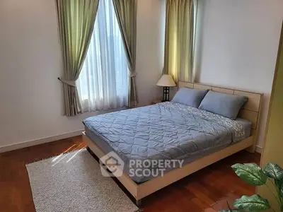 Cozy bedroom with natural light, wooden flooring, and elegant curtains.