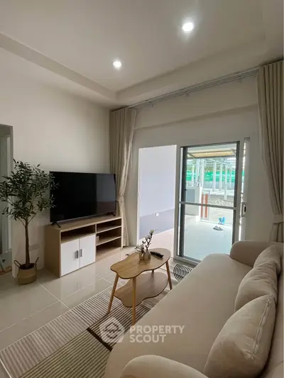 Modern living room with cozy sofa and large TV, leading to a spacious balcony.