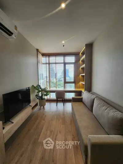 Modern living room with large window and city view, featuring a cozy sofa and sleek TV setup.
