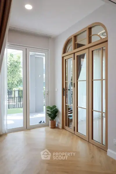 Bright and airy living room with elegant wooden doors and large windows opening to a balcony.