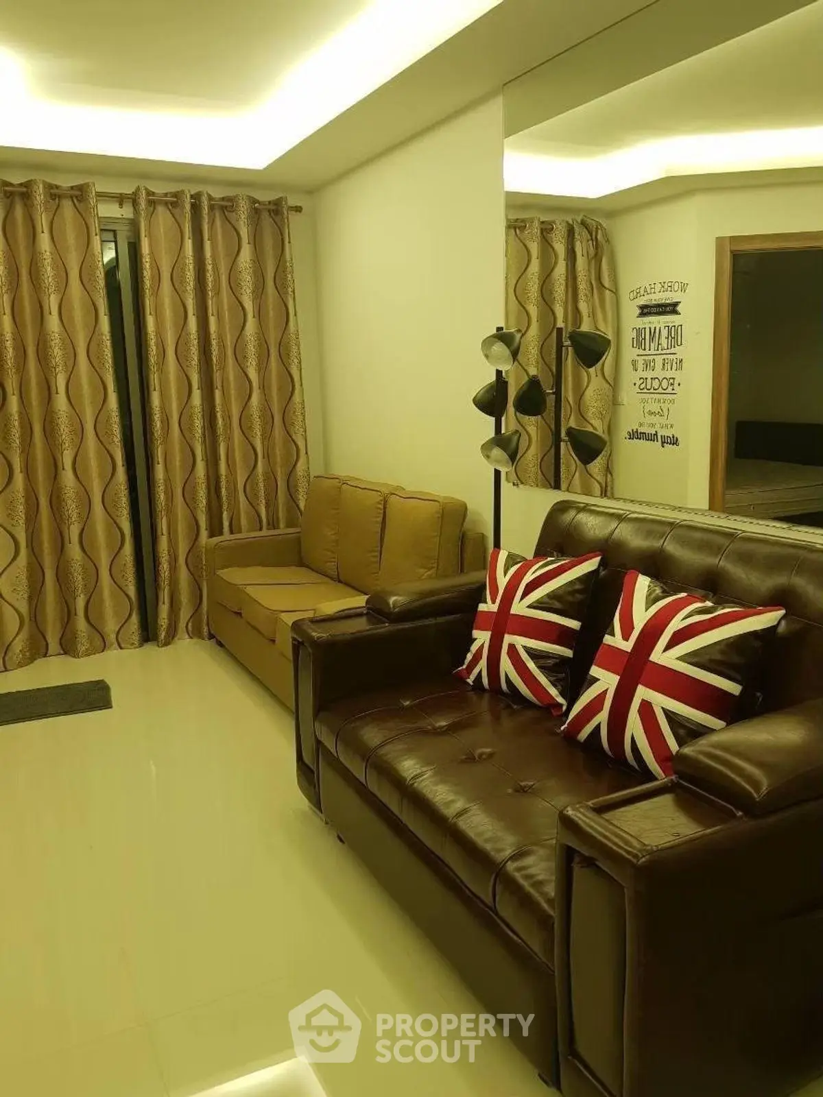 Stylish living room with leather sofa and Union Jack pillows, modern lighting, and elegant curtains.