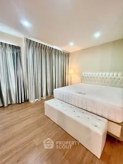 Spacious bedroom with elegant curtains and modern lighting, featuring a plush bed and wooden flooring.