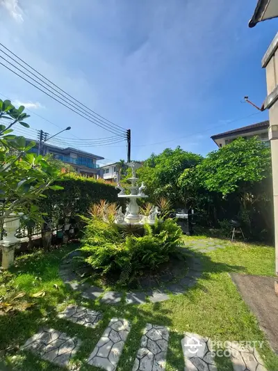 Charming garden with elegant fountain and lush greenery under clear blue sky.