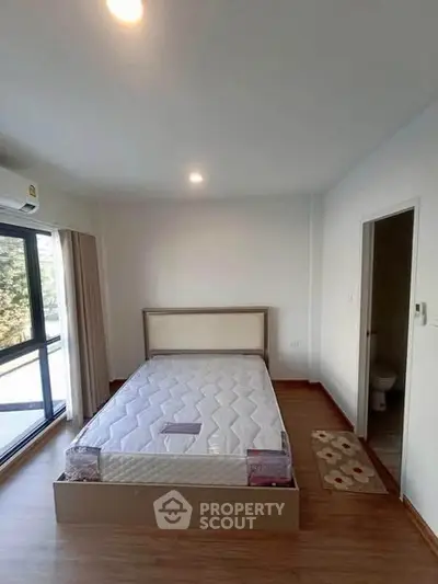 Spacious bedroom with large window and en-suite bathroom in modern apartment.
