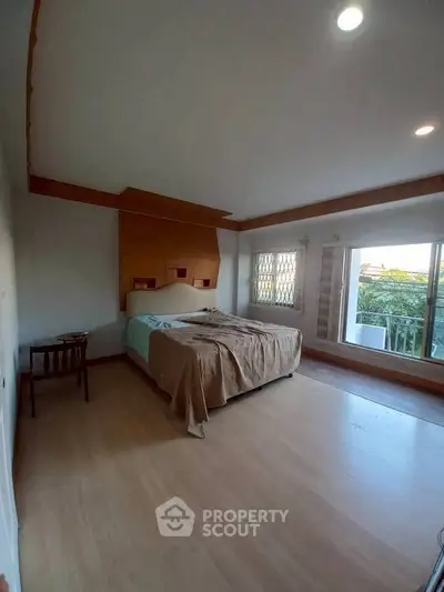 Spacious bedroom with large windows and natural light, featuring a cozy bed and wooden flooring.
