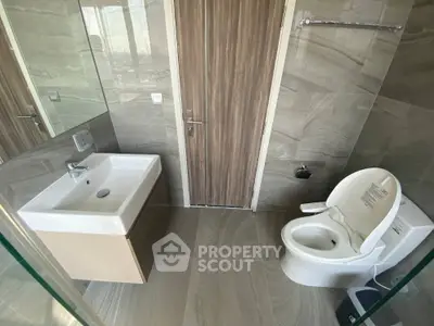 Modern bathroom with sleek fixtures and neutral tones, featuring a sink and toilet.