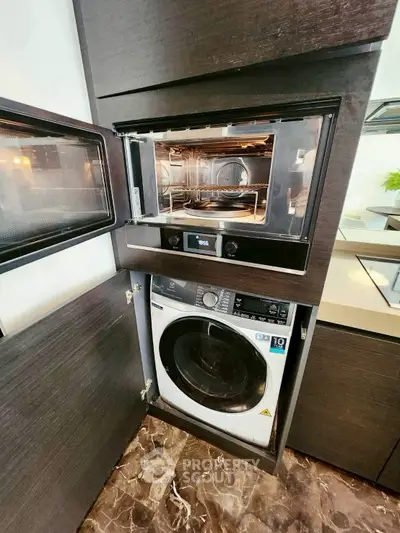 Modern kitchen with built-in oven and washing machine, sleek dark cabinetry, and marble flooring.