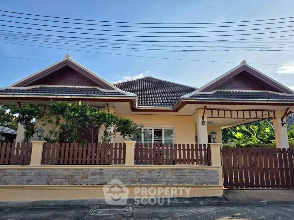 Charming single-story house with a tiled roof and wooden fence, surrounded by lush greenery.