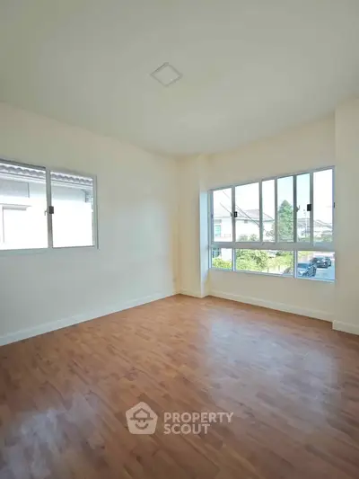 Spacious empty room with wooden flooring and large windows offering natural light.