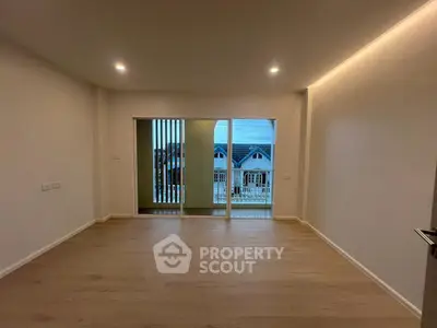 Spacious empty room with wooden flooring and large windows offering a scenic view of neighboring houses.