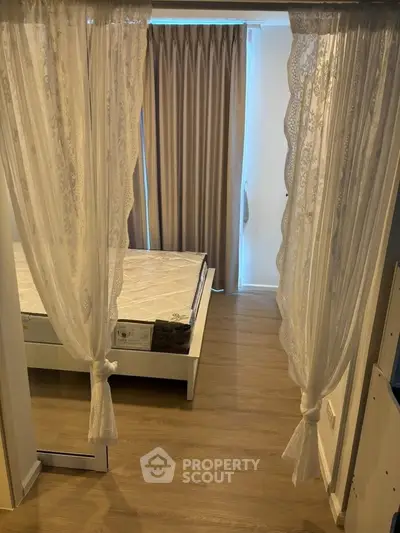 Cozy bedroom with elegant lace curtains and wooden flooring, perfect for a serene retreat.
