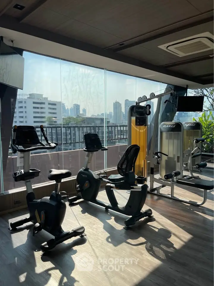 Modern gym with city view, featuring exercise bikes and fitness equipment in a bright, spacious setting.