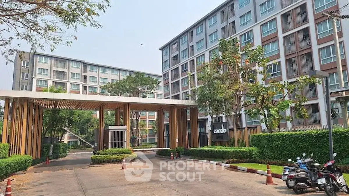 Modern apartment complex entrance with lush greenery and contemporary design.