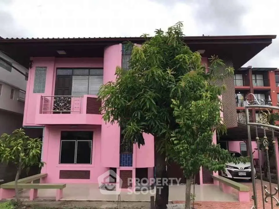 Charming pink two-story house with lush greenery and modern design elements.
