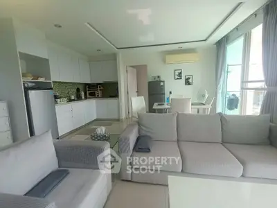 Modern open-layout living room with kitchen, featuring sleek furniture and natural light.