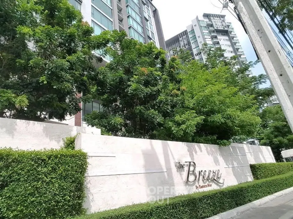 Modern condominium building with lush greenery and stylish entrance signage.