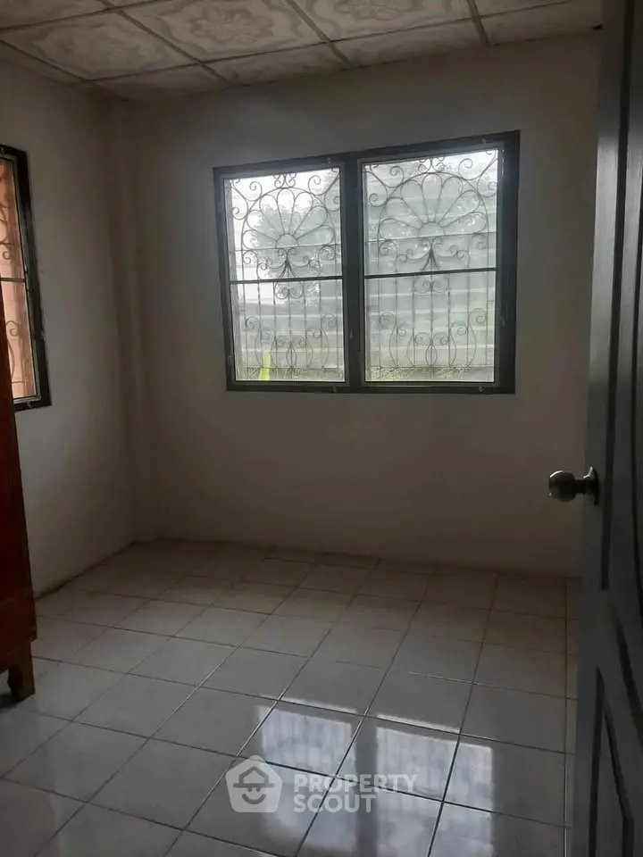 Spacious empty room with tiled floor and decorative window grills.