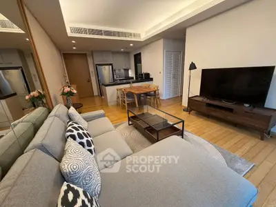 Modern living room with stylish decor and open kitchen layout, featuring a cozy sofa and large TV.