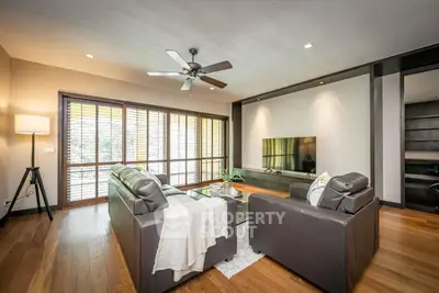 Luxurious living room with modern leather sofas and large TV, featuring elegant wooden flooring and ceiling fan.