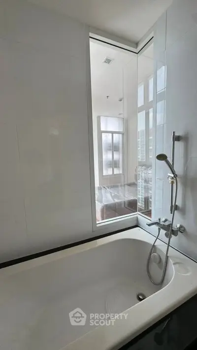 Modern bathroom with sleek bathtub and large window offering natural light.