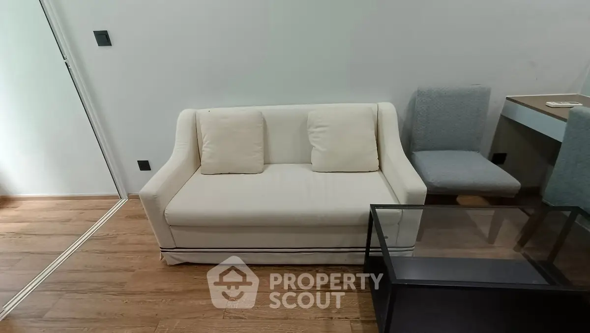 Cozy living room with modern sofa and glass coffee table on wooden floor.