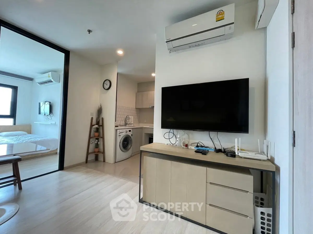 Modern apartment interior with open living area, TV, and kitchen appliances.