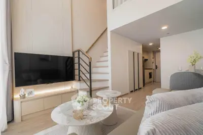 Modern duplex living room with stylish decor and staircase, featuring a sleek TV setup and elegant furniture.