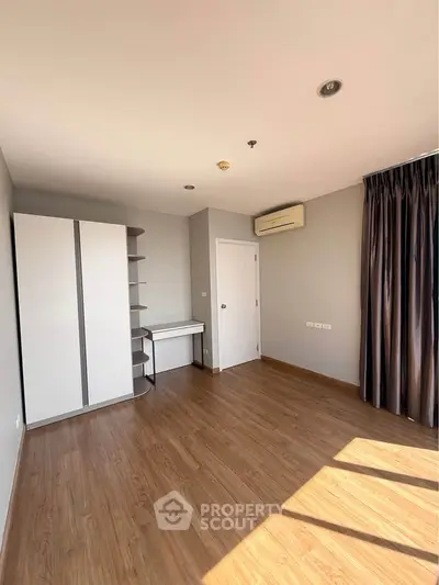Spacious bedroom with wooden flooring and ample natural light, featuring a built-in wardrobe and desk.