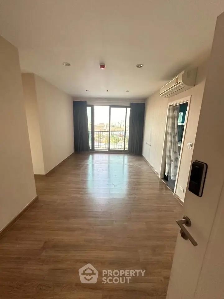 Spacious empty room with wooden flooring and large windows offering natural light and city view.