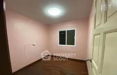 Cozy empty room with wooden flooring and pink walls, perfect for a bedroom or study.
