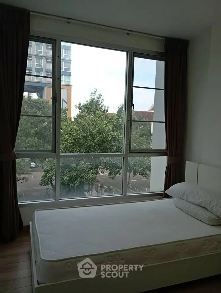 Cozy bedroom with large window offering a serene view of trees and cityscape.