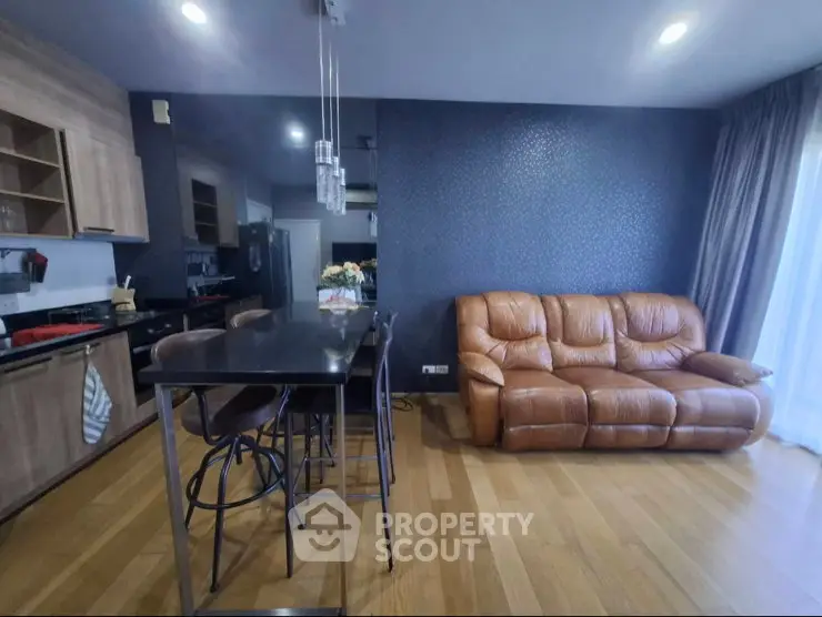 Modern open-layout living room with kitchen, featuring leather sofa and sleek bar counter.