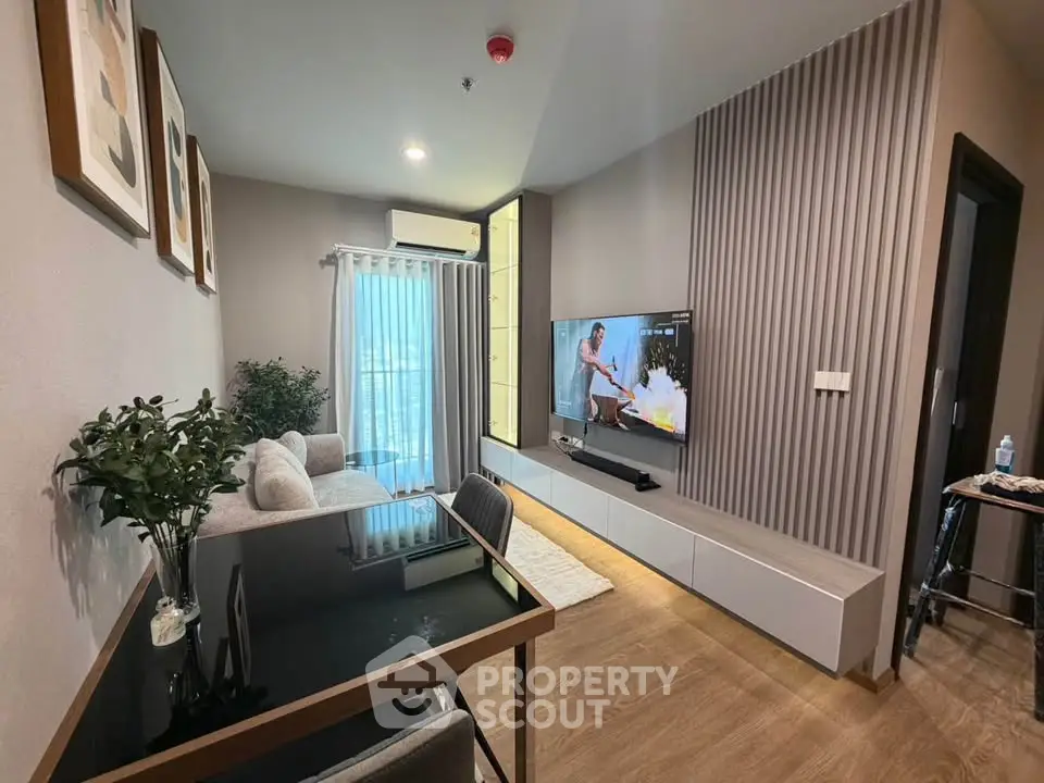 Modern living room with stylish decor, large TV, and natural light from balcony window.