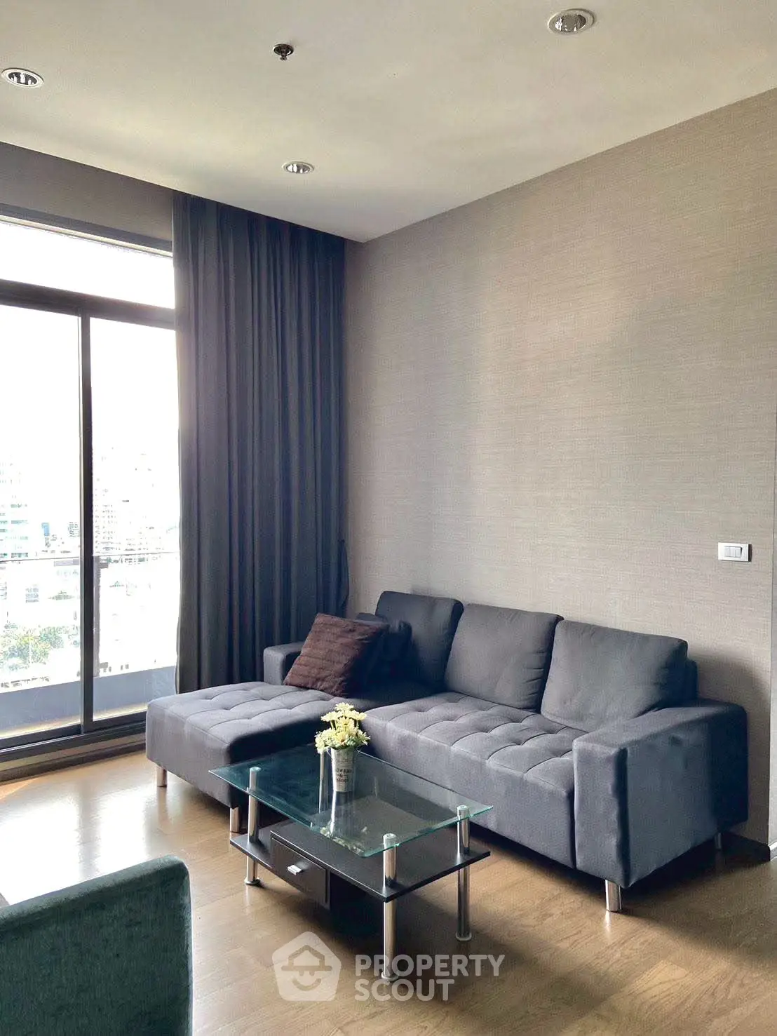Modern living room with stylish gray sofa and glass coffee table, featuring large window with city view.