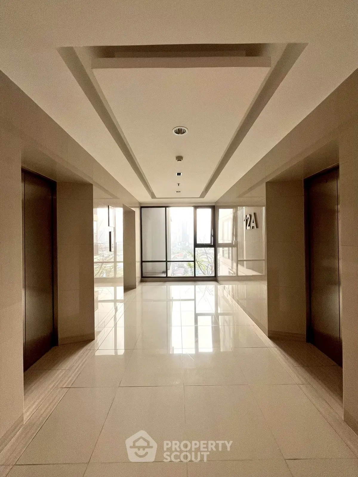 Modern building corridor with elevators and large windows offering natural light.