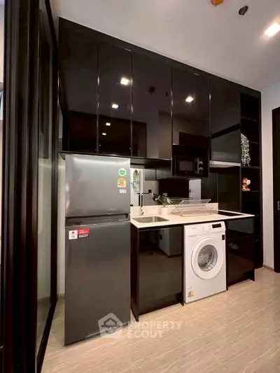 Modern kitchen with sleek black cabinets, stainless steel fridge, and washing machine.