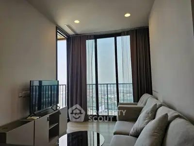 Modern living room with large windows offering stunning city views, featuring a cozy sofa and sleek TV setup.
