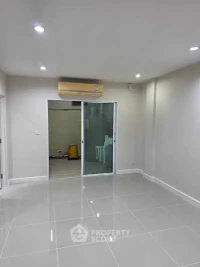 Spacious empty room with glossy tiled floor and sliding glass door, ideal for customization.
