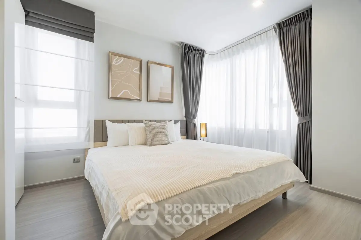 Modern bedroom with large windows and stylish decor, featuring elegant curtains and cozy bedding.