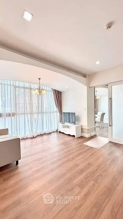 Spacious living room with wooden flooring and natural light, featuring modern furniture and elegant decor.